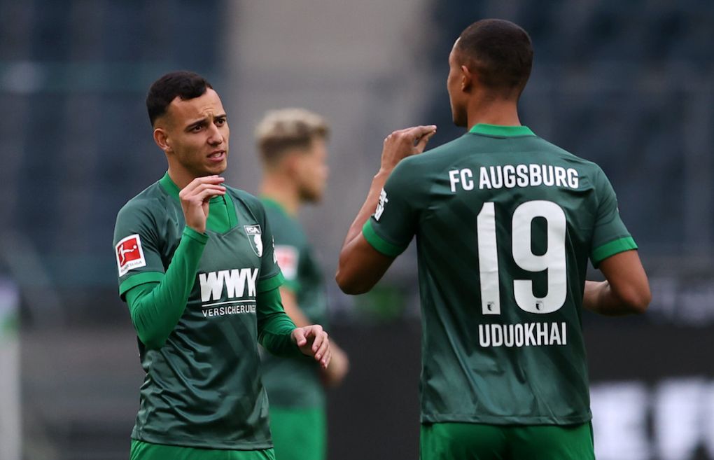 MOENCHENGLADBACH, GERMANY - NOVEMBER 21: Iago of Augsburg talks to teammate Felix Uduokhai during the Bundesliga match between Borussia Moenchengladbach and FC Augsburg at Borussia-Park on November 21, 2020 in Moenchengladbach, Germany. Football Stadiums around Europe remain empty due to the Coronavirus Pandemic as Government social distancing laws prohibit fans inside venues resulting in fixtures being played behind closed doors. (Photo by Lars Baron/Getty Images)