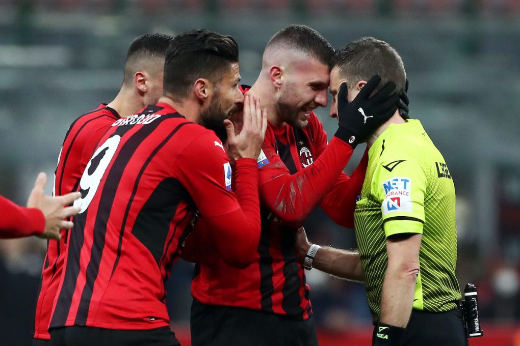 Referee Marco Serra is surrounded by AC Milan players